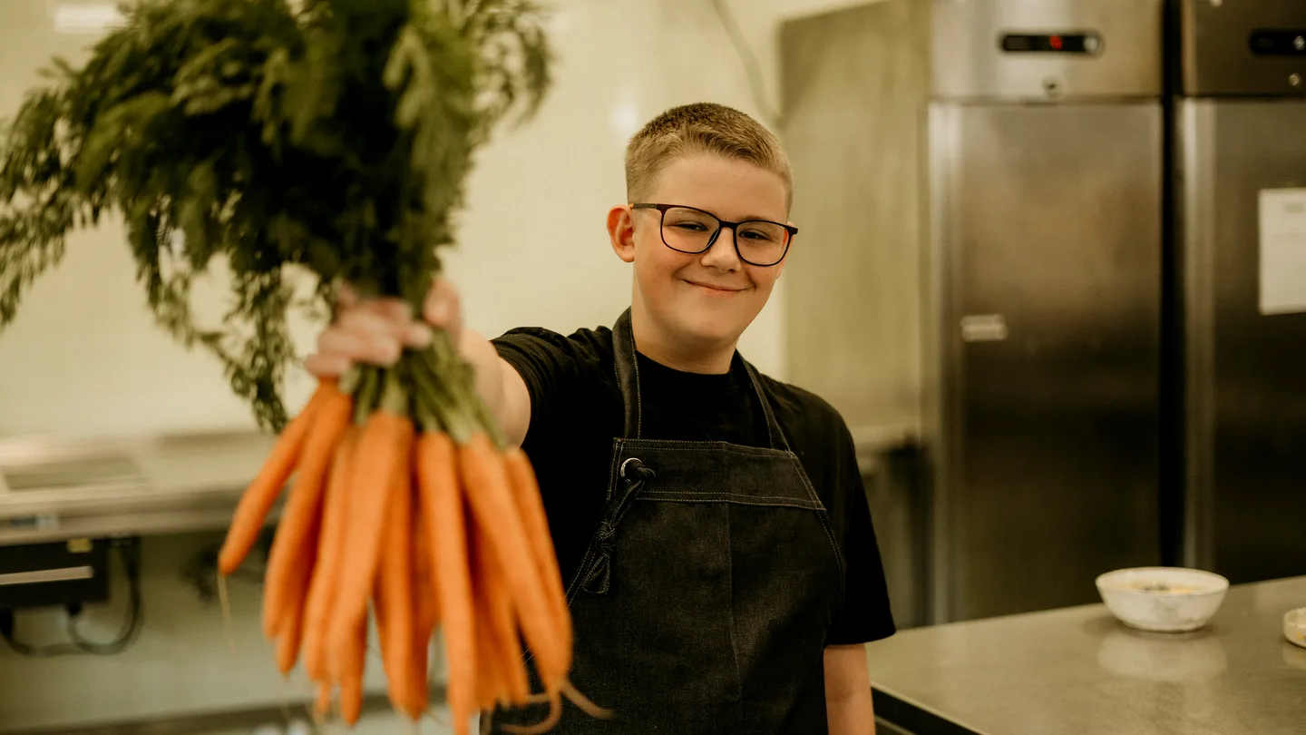 Lachende leerling met een bos wortels in de keuken