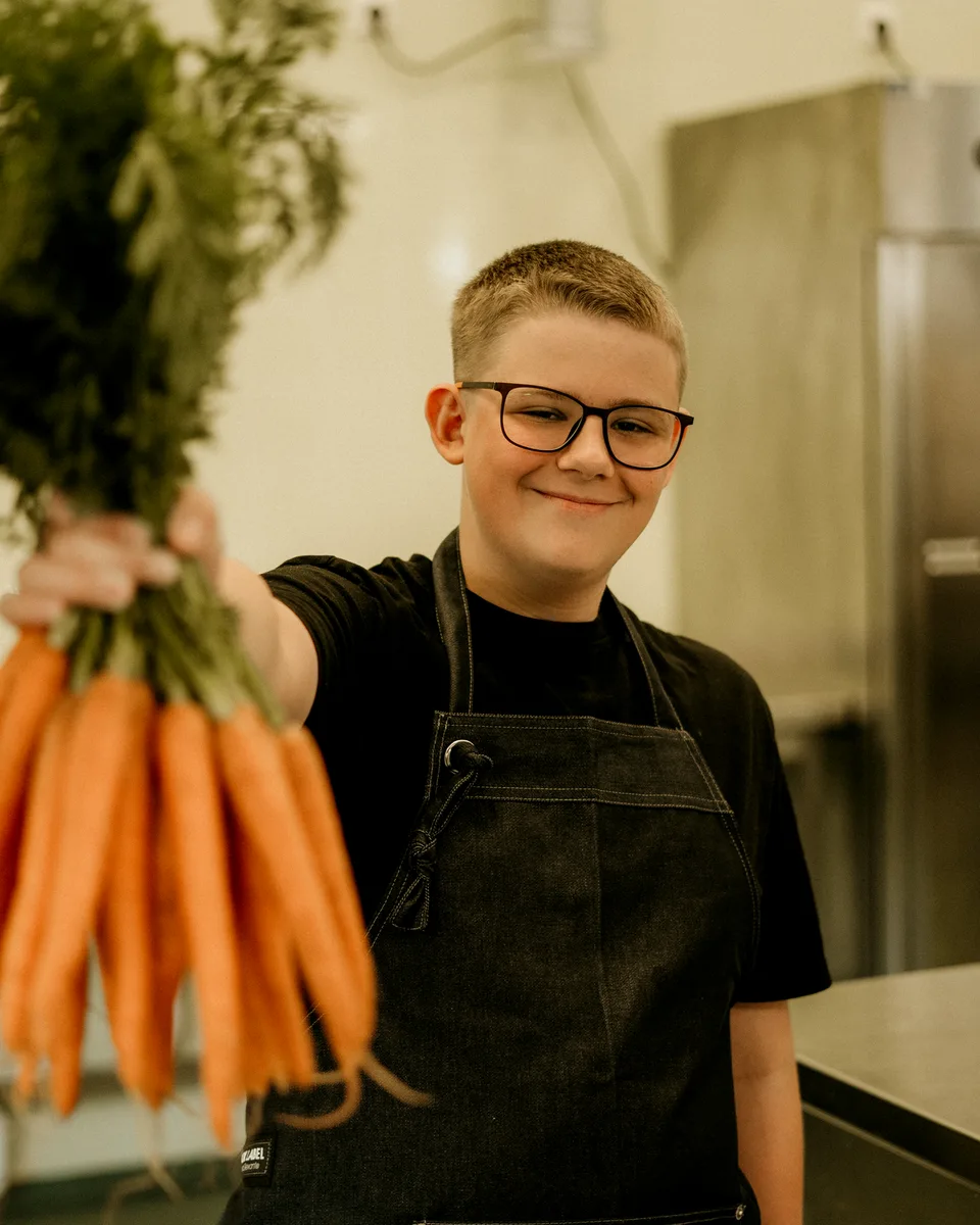 Lachende leerling met een bos wortels in de keuken